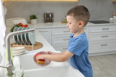 Photo of Little helper. Cute boy washing dishes at home