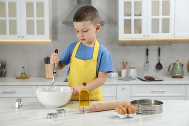 Photo of Little helper. Cute boy making dough for cookies in kitchen at home