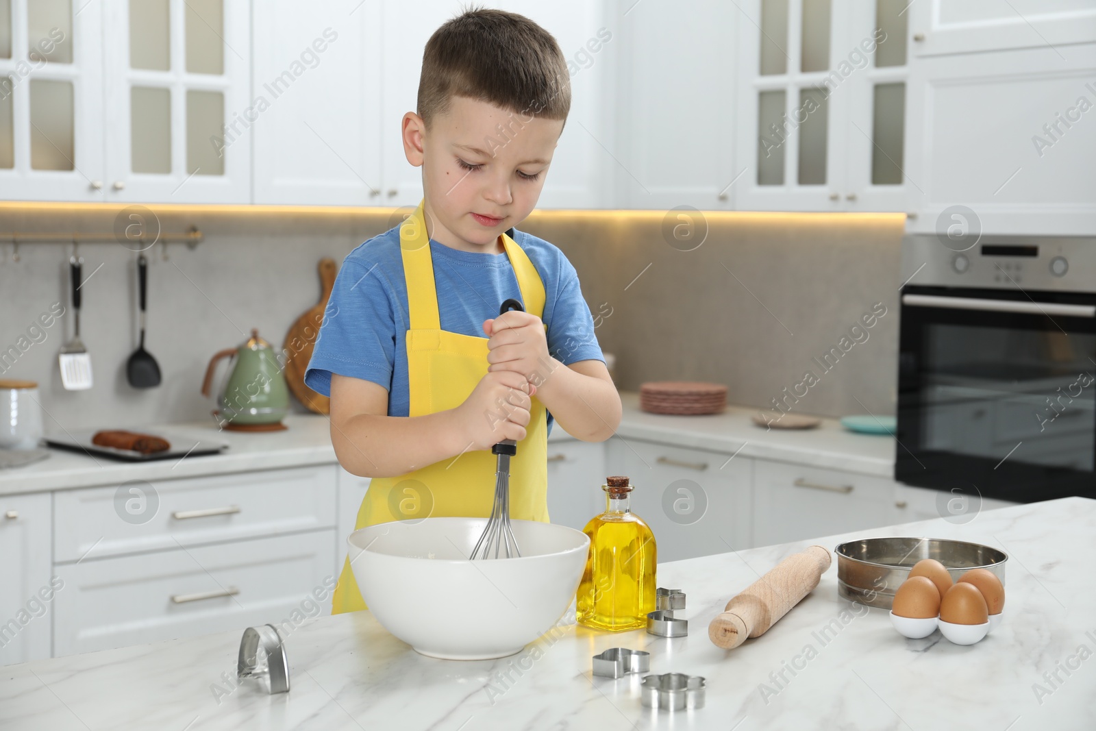 Photo of Little helper. Cute boy making dough for cookies in kitchen at home