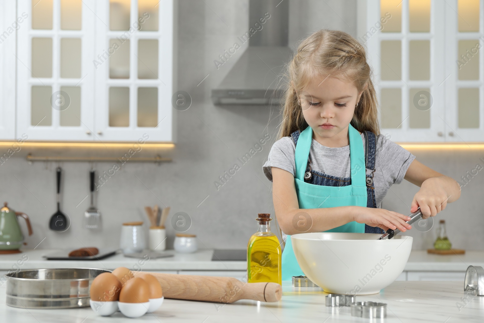 Photo of Little helper. Cute girl making dough for cookies in kitchen at home, space for text