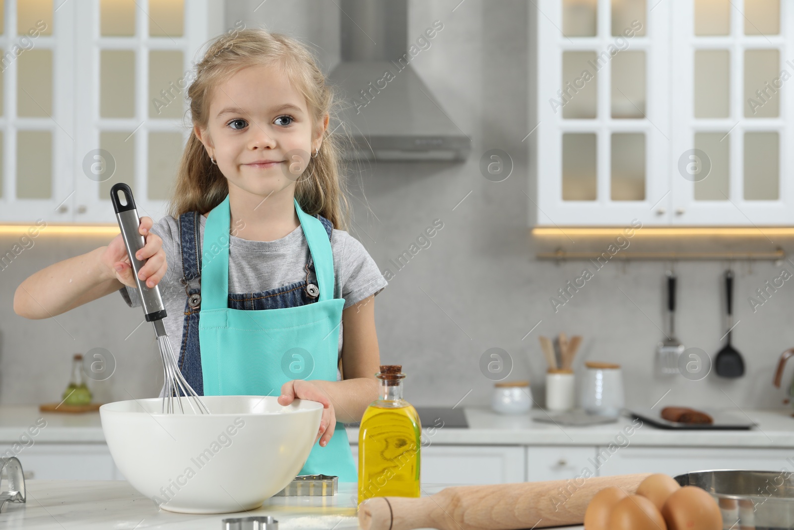 Photo of Little helper. Cute girl making dough for cookies in kitchen at home, space for text