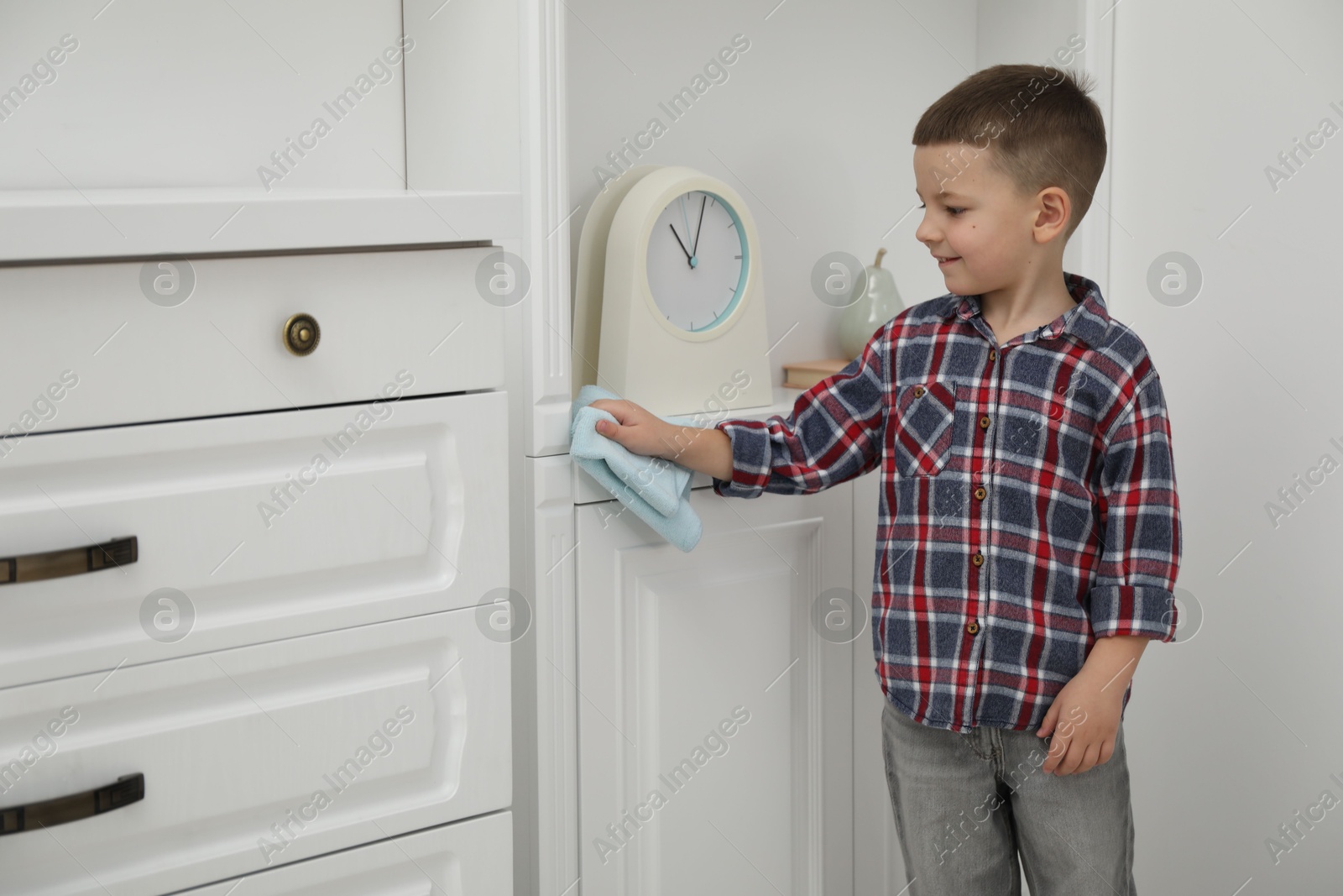 Photo of Little helper. Cute boy wiping dust from furniture at home