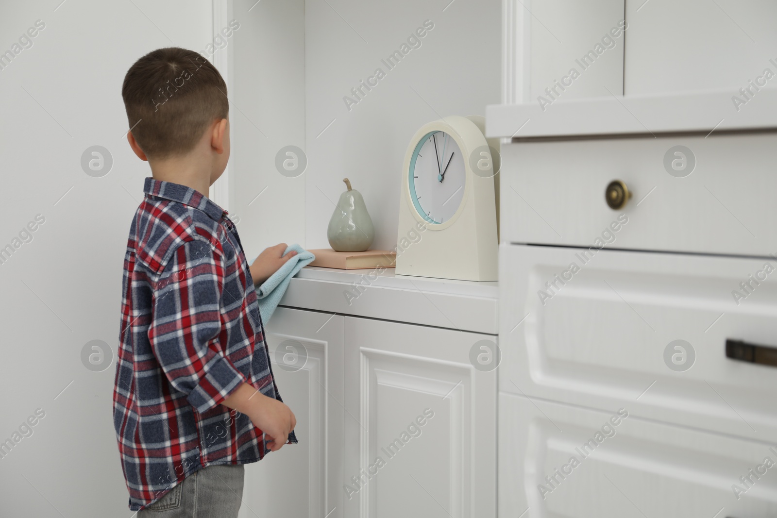 Photo of Little helper. Cute boy wiping dust from furniture at home