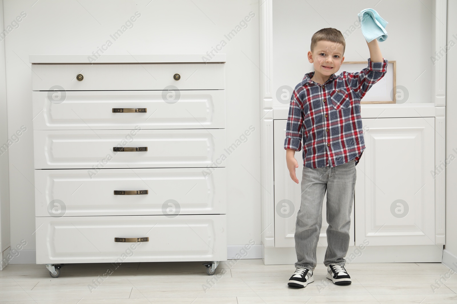 Photo of Little helper. Cute boy wiping dust at home