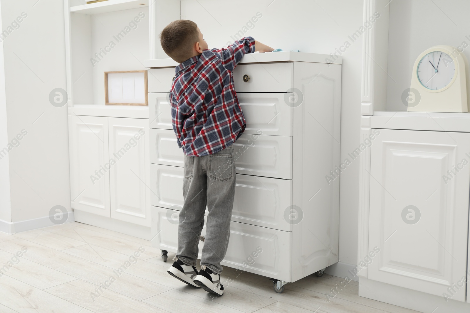 Photo of Little helper. Cute boy wiping dust from chest of drawers at home, back view