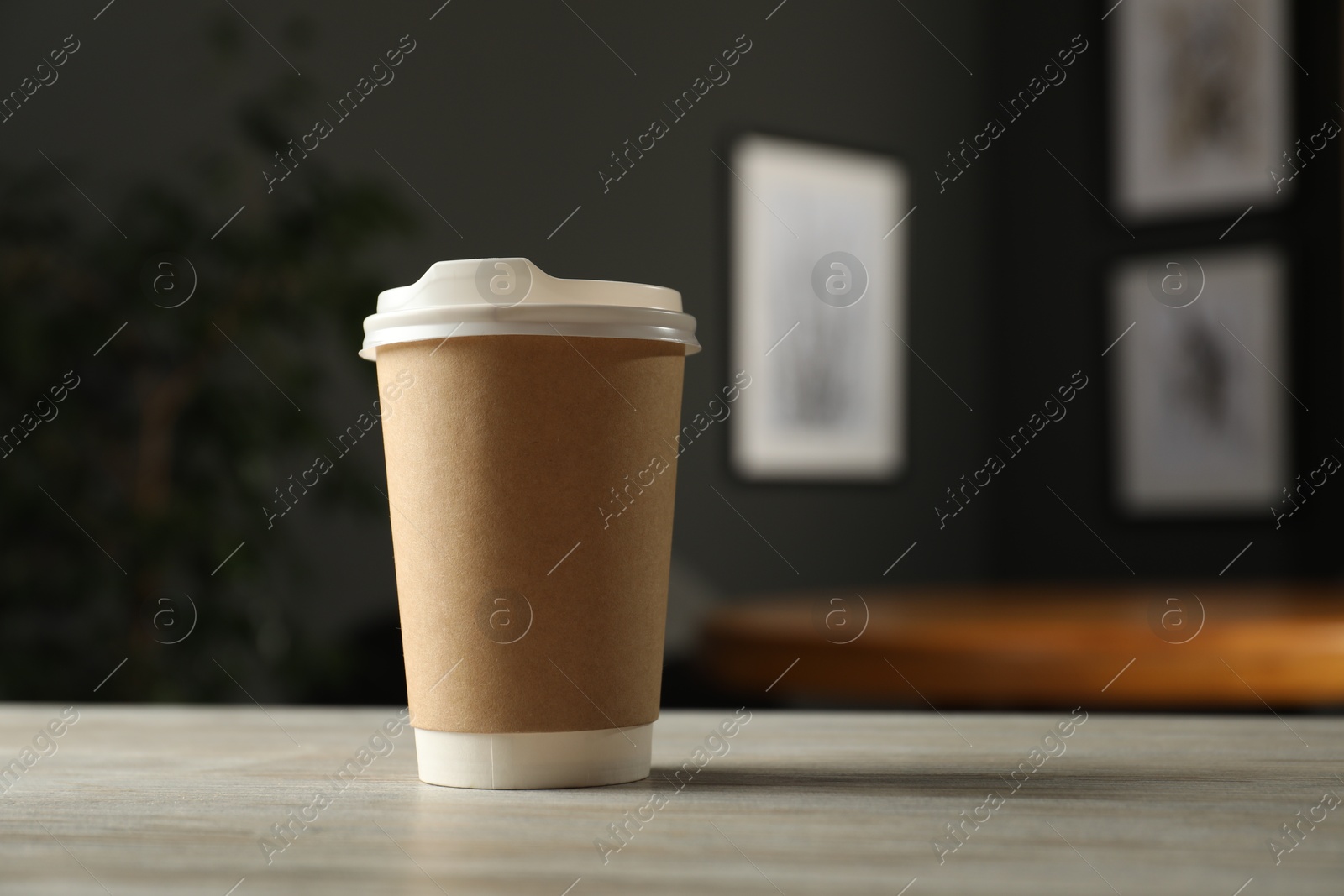 Photo of Paper cup on light wooden table in cafe, closeup. Mockup for design