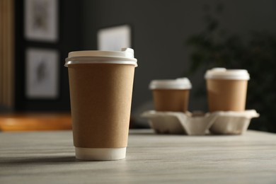 Photo of Paper cup on light wooden table in cafe, closeup. Mockup for design