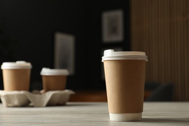 Photo of Paper cup on light wooden table in cafe, closeup. Mockup for design