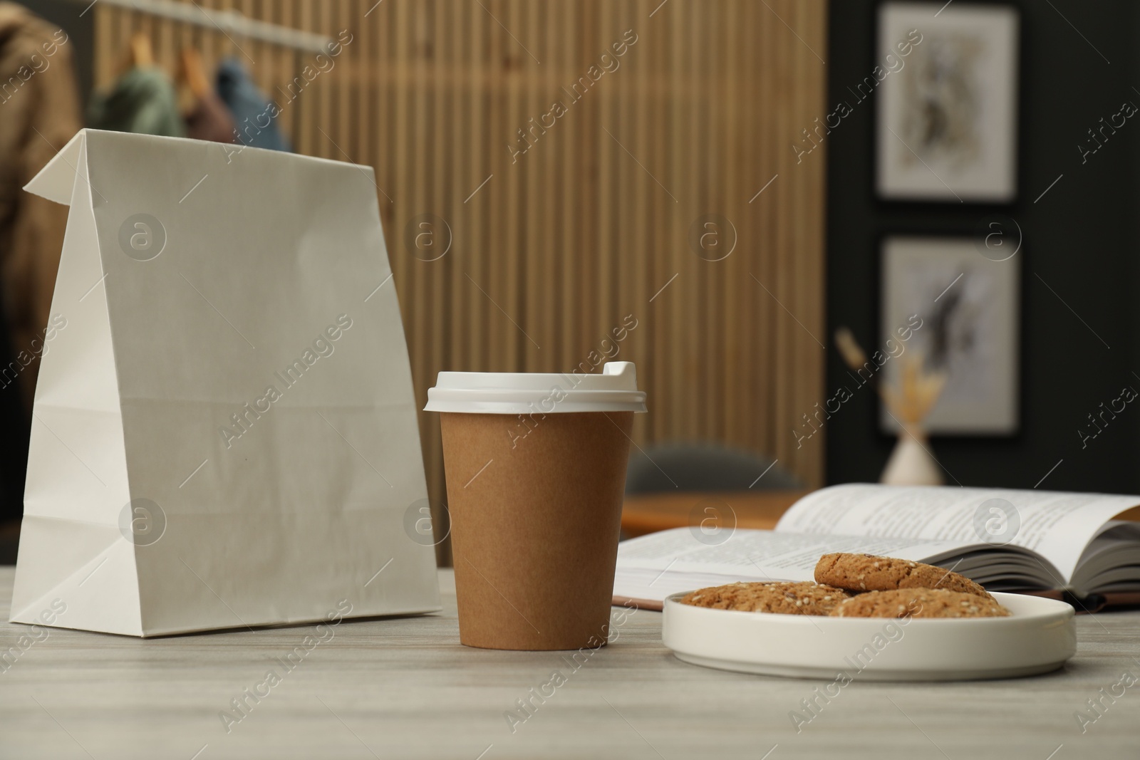 Photo of Paper cup, plate of cookies, book and takeaway bag on light wooden table in cafe. Mockup for design