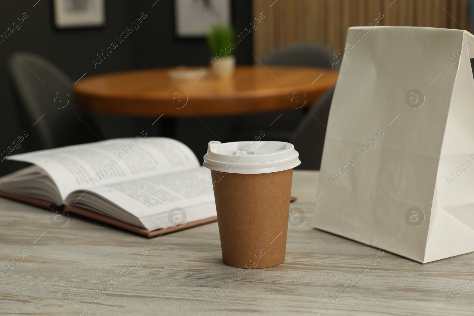 Photo of Paper cup, book and takeaway bag on light wooden table in cafe. Mockup for design