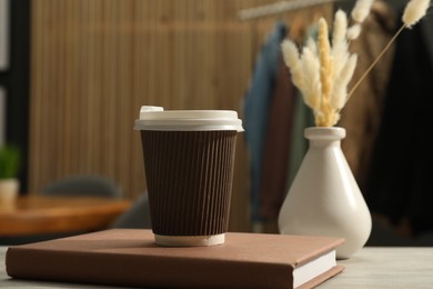 Photo of Paper cup, book and spikelets in vase on light wooden table in cafe, closeup. Mockup for design