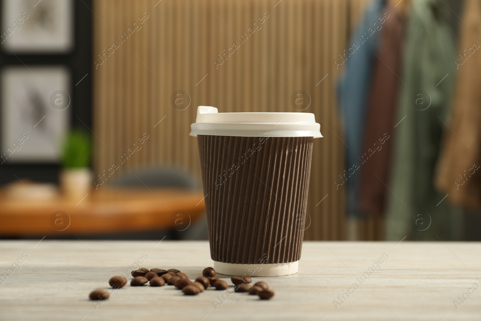 Photo of Paper cup and coffee beans on light wooden table indoors, closeup. Mockup for design