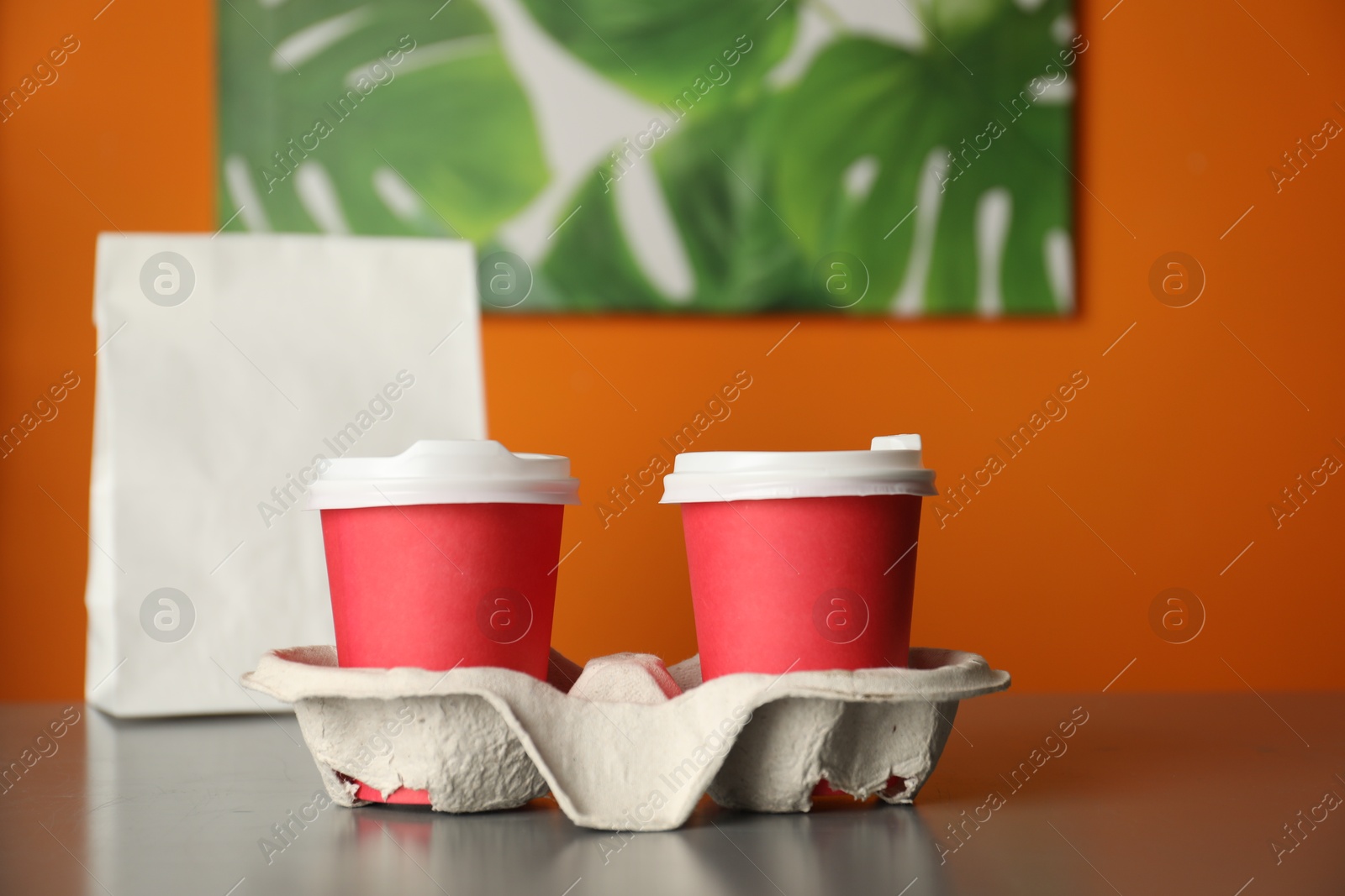 Photo of Holder with paper cups on grey table in cafe, closeup. Mockup for design