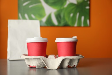 Photo of Holder with paper cups on grey table in cafe, closeup. Mockup for design