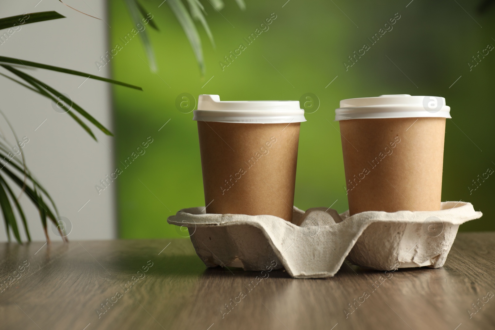 Photo of Holder with paper cups on wooden table in cafe, closeup. Mockup for design