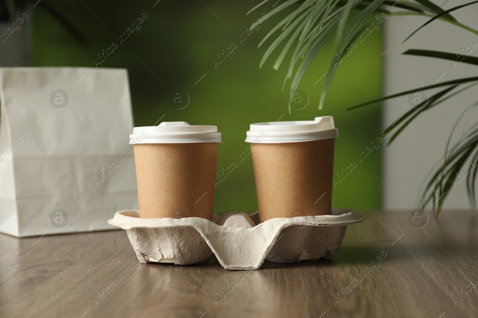 Photo of Holder with paper cups on wooden table in cafe, closeup. Mockup for design