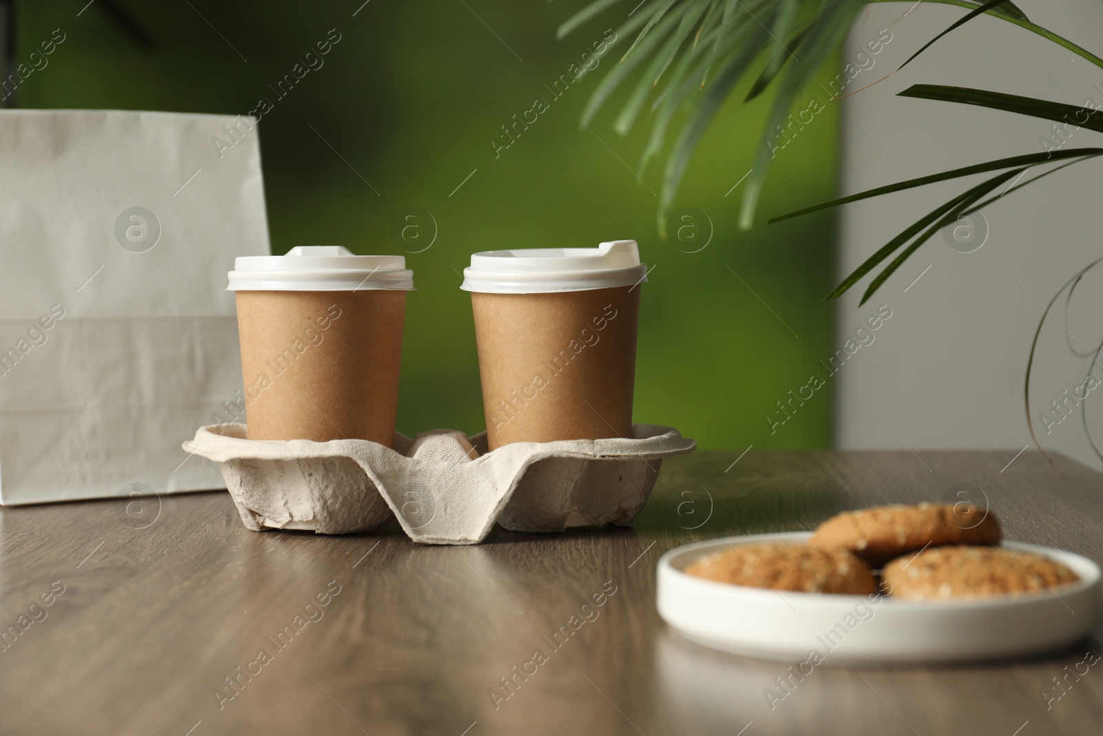 Photo of Holder with paper cups and plate of cookies on wooden table in cafe. Mockup for design