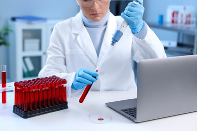 Laboratory testing. Doctor dripping blood sample into test tube at table indoors, closeup