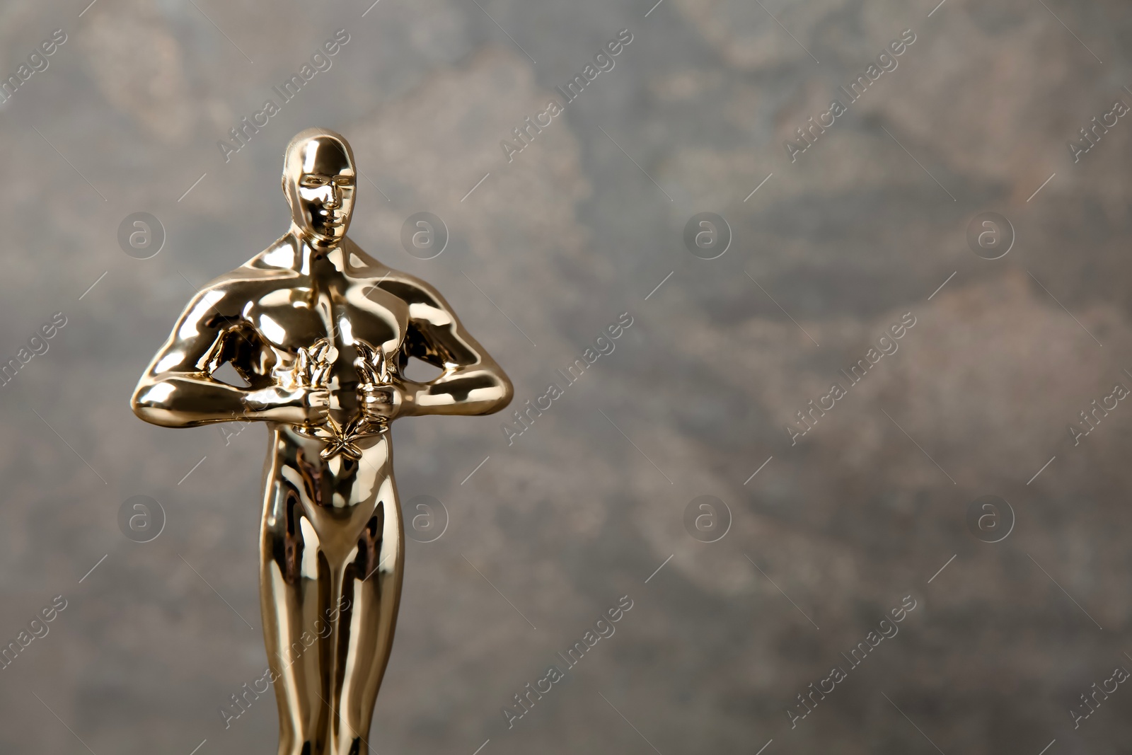 Photo of Golden trophy in shape of human figure against blurred gray background, space for text