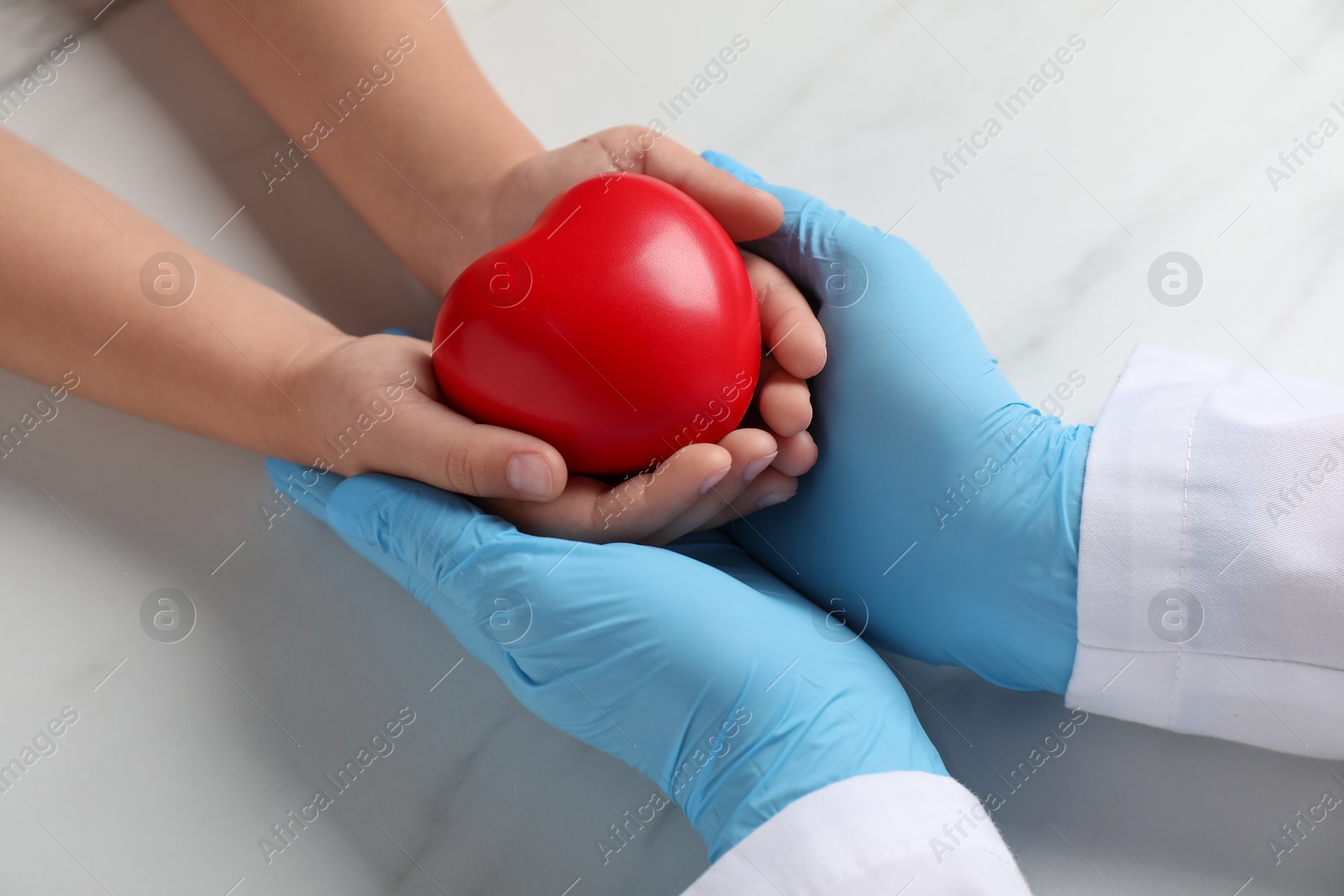 Photo of Doctor and child with heart model at white marble table, closeup