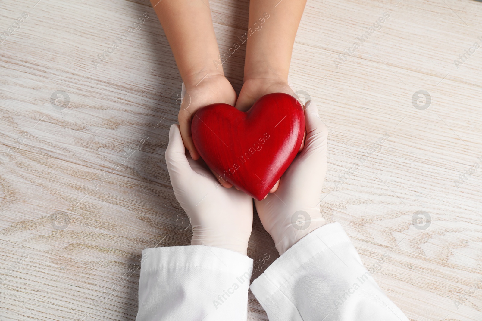 Photo of Doctor and child with heart model at white wooden table, top view