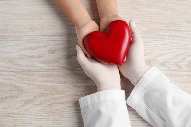 Photo of Doctor and child with heart model at white wooden table, top view