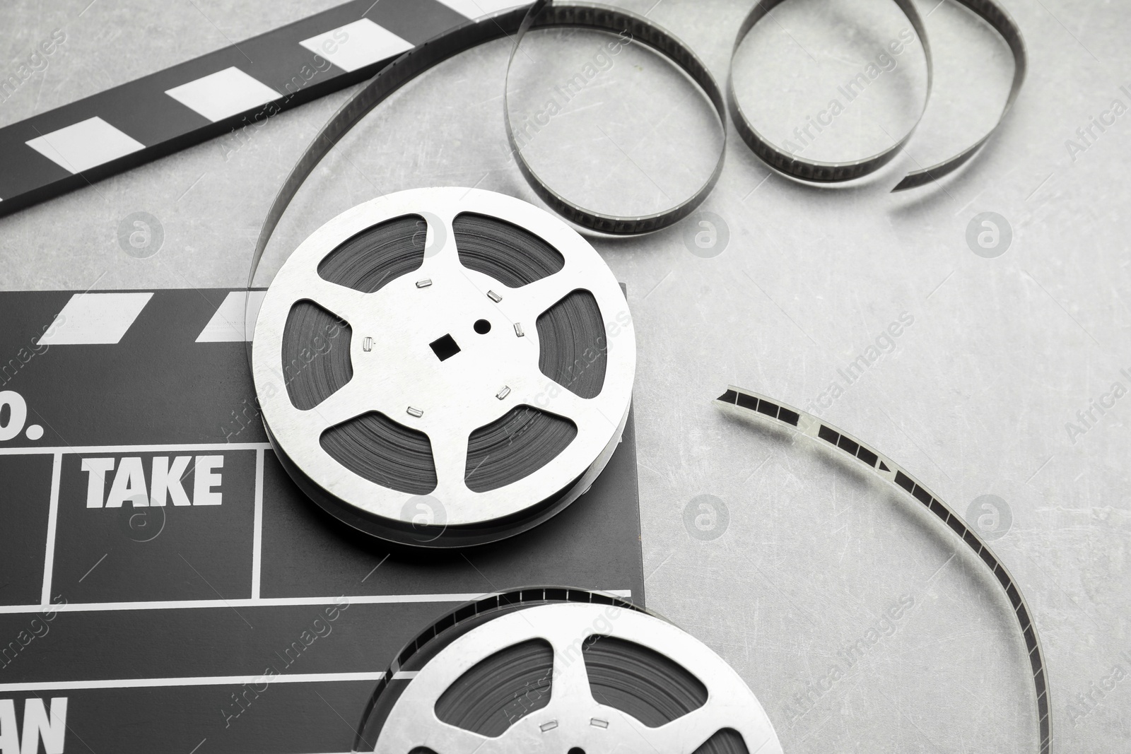 Photo of Movie clapper and film reels on grey textured table, closeup