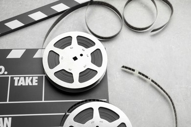 Photo of Movie clapper and film reels on grey textured table, closeup