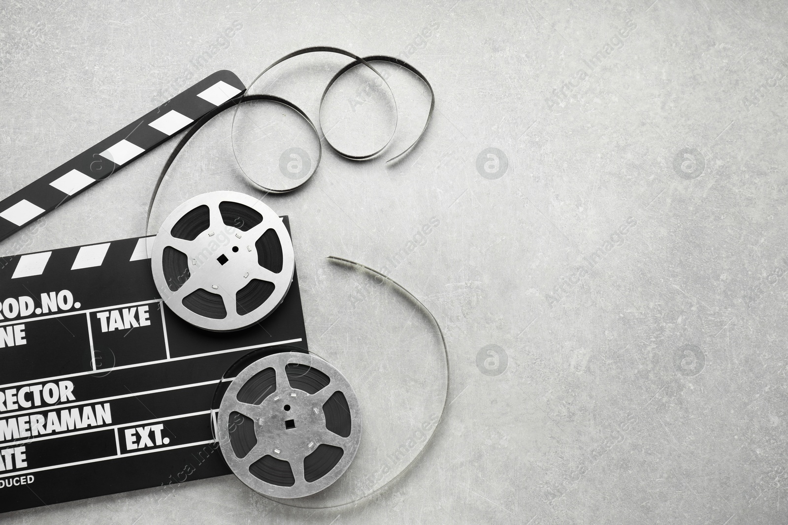 Photo of Movie clapper and film reels on grey textured table, top view. Space for text