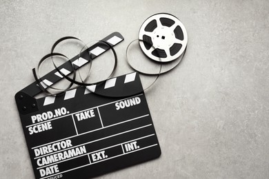 Photo of Movie clapper and film reel on grey textured table, flat lay