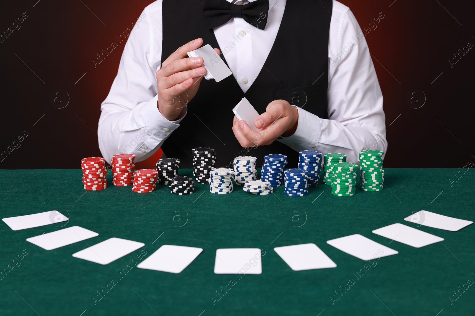 Photo of Professional croupier shuffling cards at gambling table against dark red background, closeup