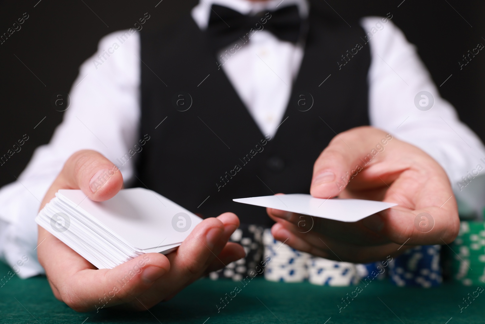 Photo of Professional croupier with playing cards at gambling table, closeup