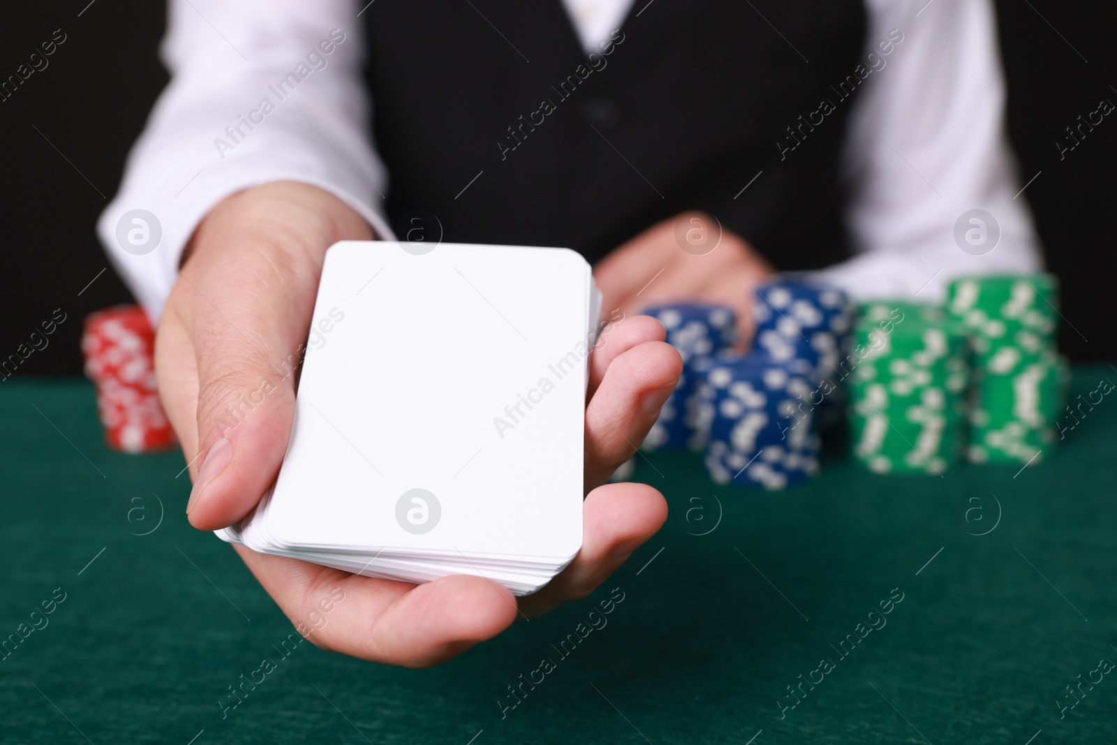 Photo of Professional croupier with playing cards at gambling table, closeup