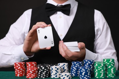 Photo of Professional croupier with playing cards at gambling table, closeup