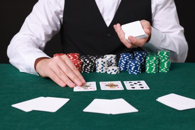 Photo of Professional croupier with playing cards at gambling table, closeup