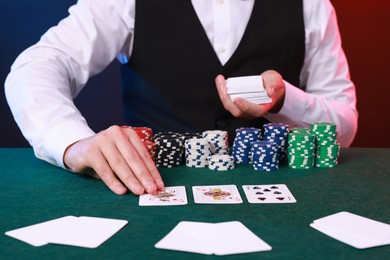 Photo of Professional croupier with playing cards at gambling table, closeup