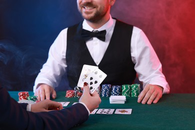 Photo of Professional croupier and gambler at table with playing cards and casino chips, closeup