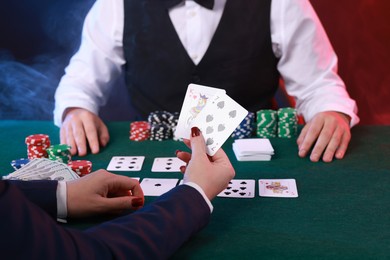 Photo of Professional croupier and gambler at table with playing cards and casino chips, closeup