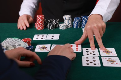 Photo of Professional croupier and gambler at table with playing cards and casino chips, closeup