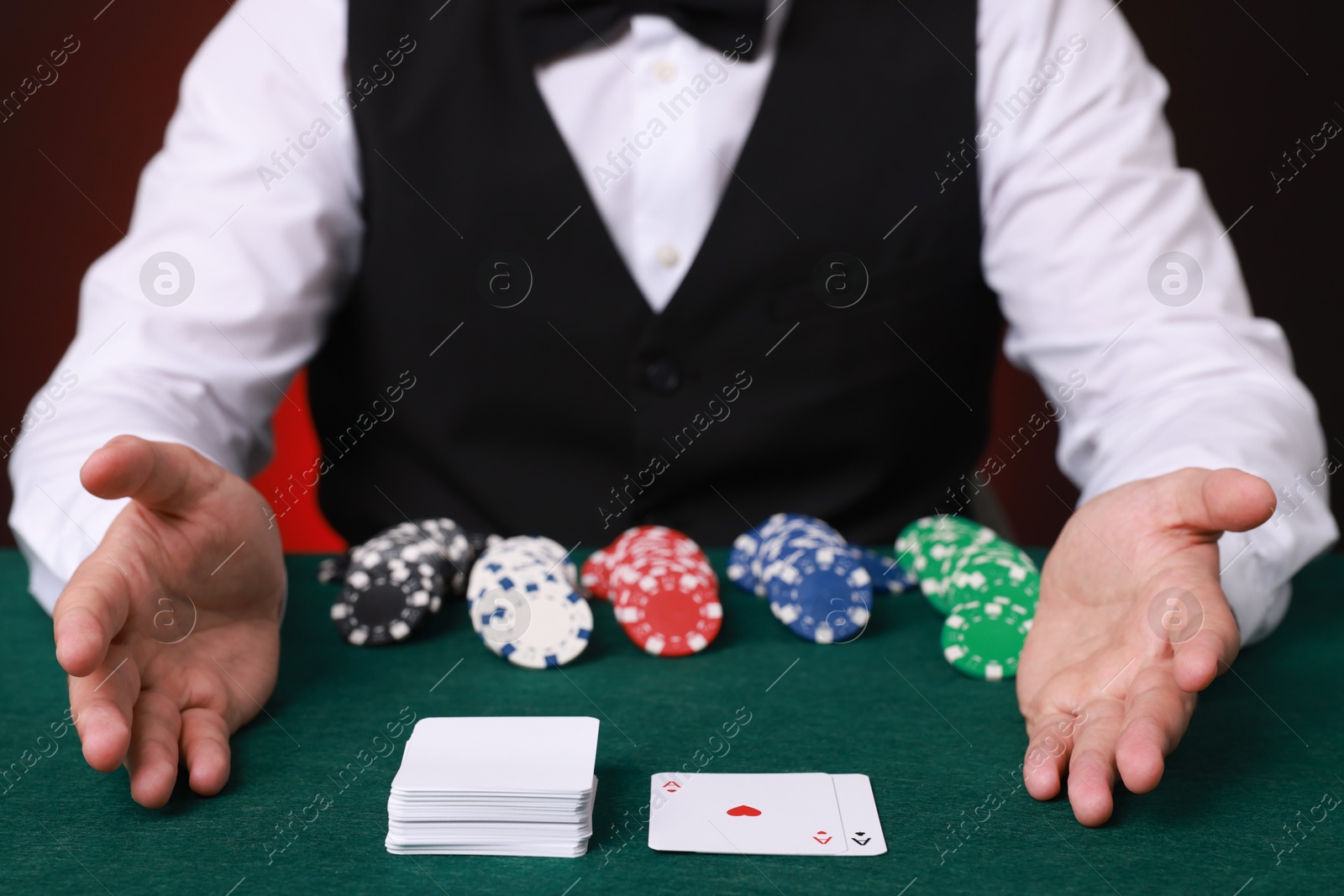 Photo of Professional croupier at gambling table with casino chips and playing cards, closeup