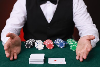 Photo of Professional croupier at gambling table with casino chips and playing cards, closeup