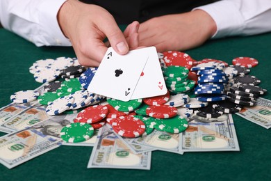 Photo of Professional croupier holding playing cards at gambling table with casino chips and money, closeup