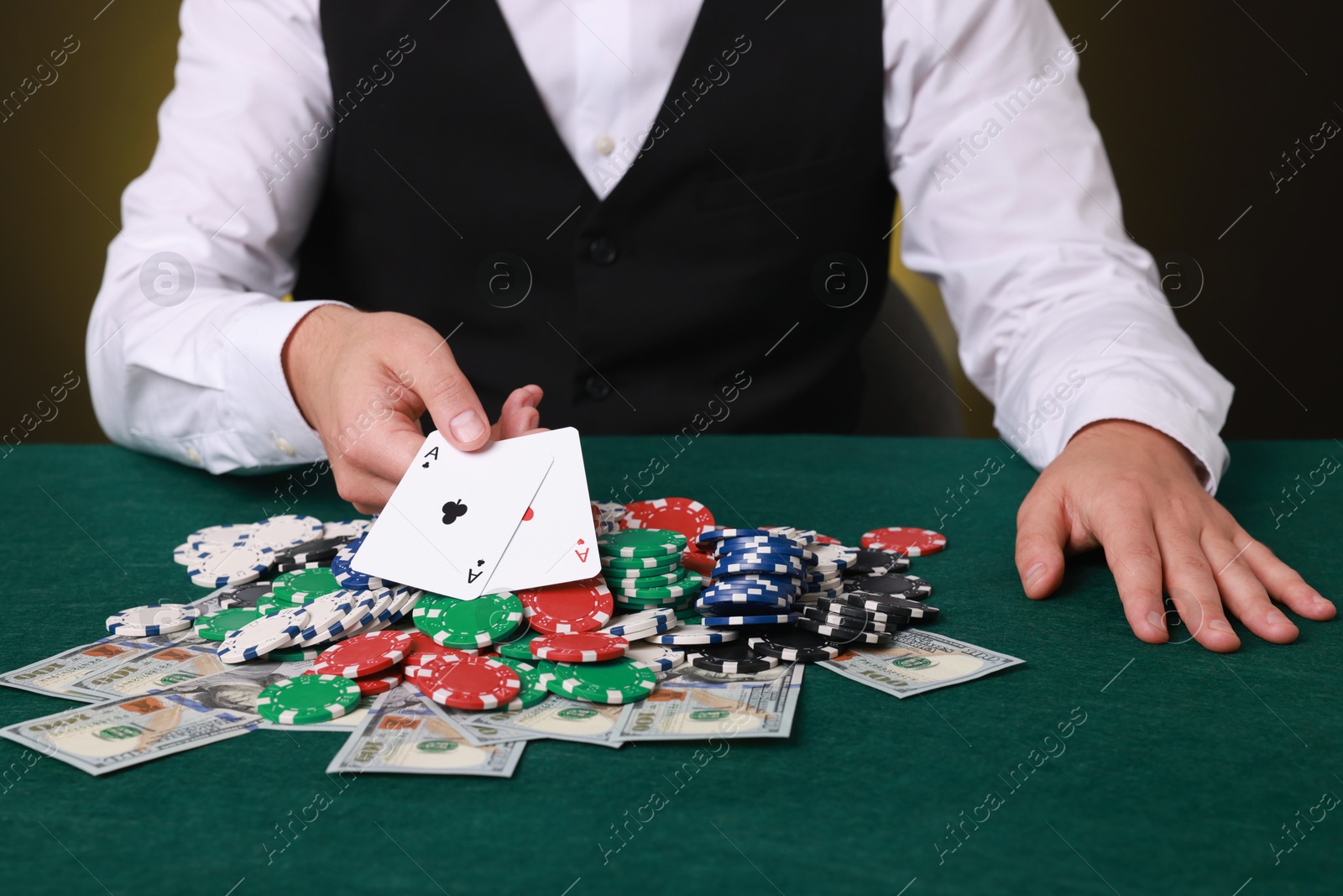 Photo of Professional croupier holding playing cards at gambling table with casino chips and money, closeup