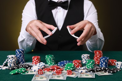 Photo of Professional croupier shuffling cards at gambling table with casino chips and money, closeup