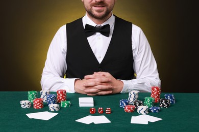 Professional croupier at gambling table with casino chips, playing cards and dice, closeup