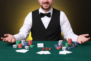 Photo of Professional croupier at gambling table with casino chips, playing cards and dice, closeup