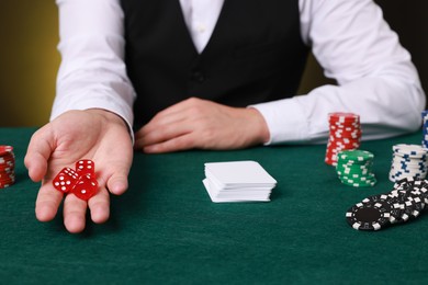 Photo of Professional croupier with dice at gambling table, closeup