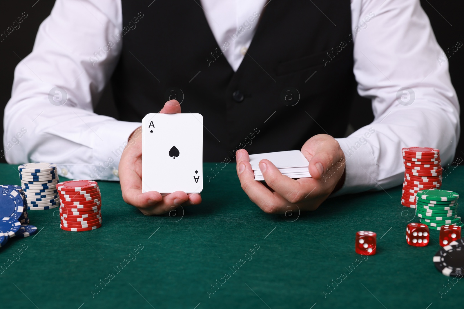 Photo of Professional croupier with playing cards at gambling table, closeup