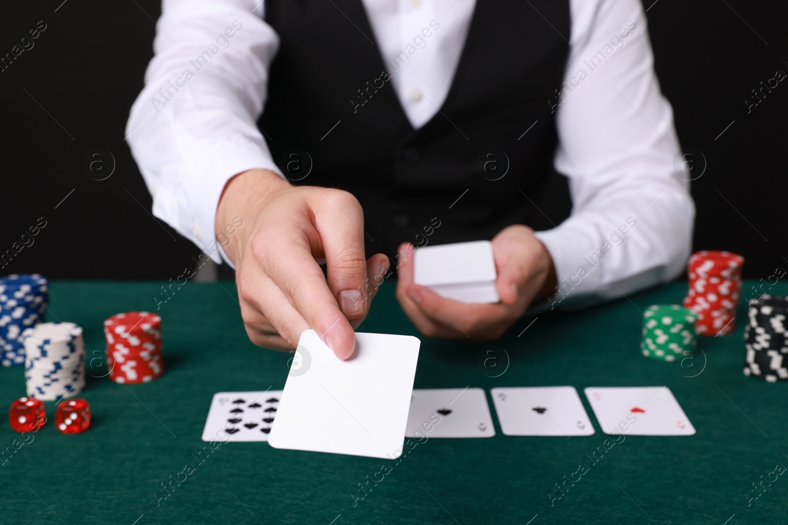 Photo of Professional croupier with playing cards at gambling table, closeup