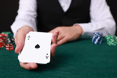 Photo of Professional croupier with playing cards at gambling table, closeup